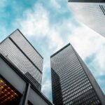 Low angle view of urban skyscrapers under a cloudy blue sky, showcasing modern architecture.