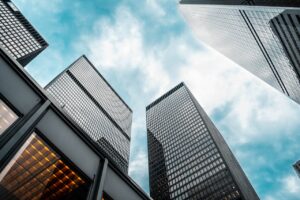 Low angle view of urban skyscrapers under a cloudy blue sky, showcasing modern architecture.
